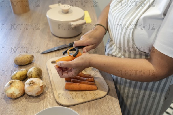 Woman peeling carrots for soup preparation in kitchen. Comfort food, homemade cooking and healthy