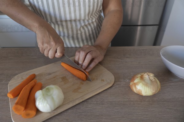 Carrot being cut with a knife on a wooden cutting board while preparing vegetables in a home
