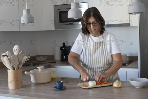 Cozy home kitchen scene with woman wearing apron cutting carrots and preparing vegetables. Comfort