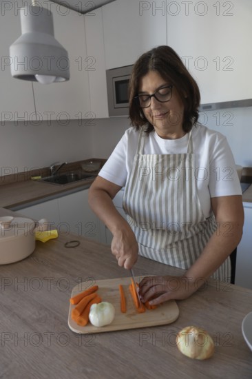 Woman cutting fresh carrots and preparing vegetables for healthy homemade meal in modern kitchen.