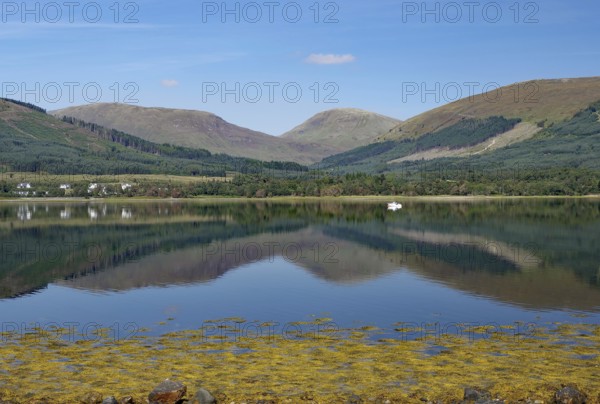 A calm body of water reflects the surrounding mountains and clear skies, Highlands, Fort William,