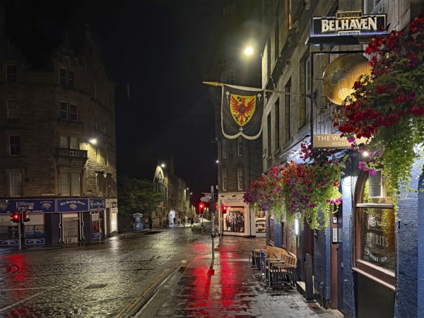 Night view of a quiet city street with wet pavement and illuminated shops. Royal Mile, Edinburgh,