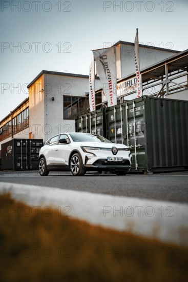 White car in front of an industrial building with containers and flags