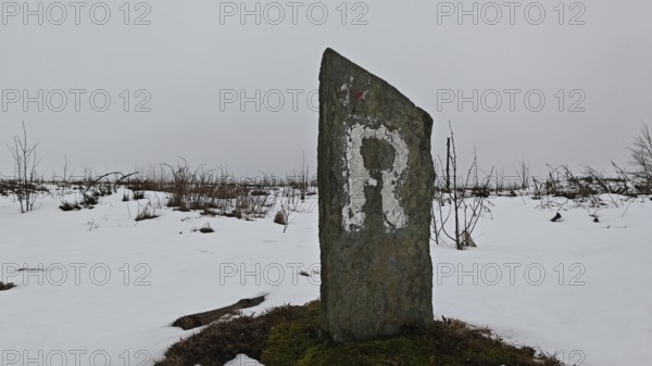 Snowy landscape with an old marker of the Rennsteig hiking trail with the letter R on it,