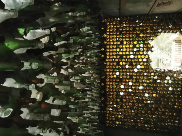 Artistic wall made of stacked glass bottles through which light shimmers, ruin house made of glass,
