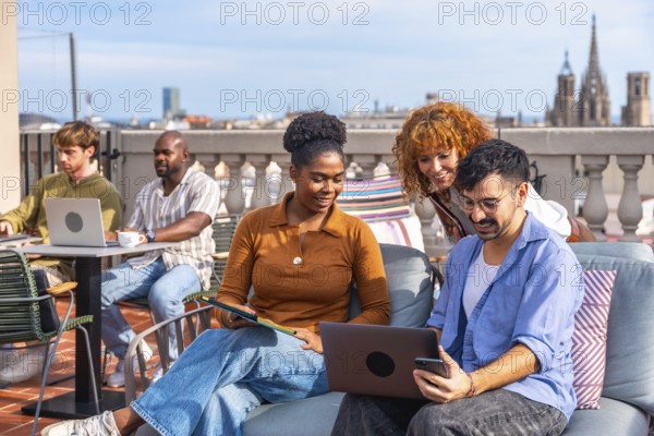 Diverse young professionals collaborating on a modern rooftop terrace, using laptops and