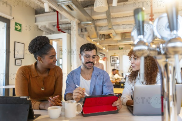 Diverse colleagues sitting at a high table, casually discussing a digital tablet and laptop during