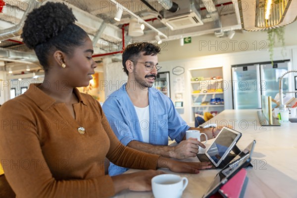 Diverse colleagues in a modern office breakroom are collaborating and discussing work using digital