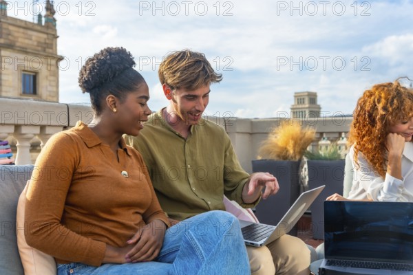 Diverse colleagues collaborate on a laptop during a rooftop meeting, sharing ideas and planning in
