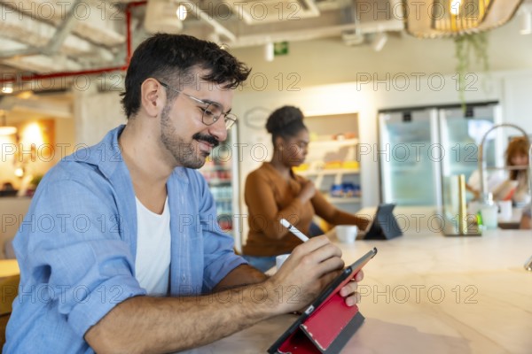 Man in casual attire smiling while using a digital tablet with a stylus to sketch ideas at a bar
