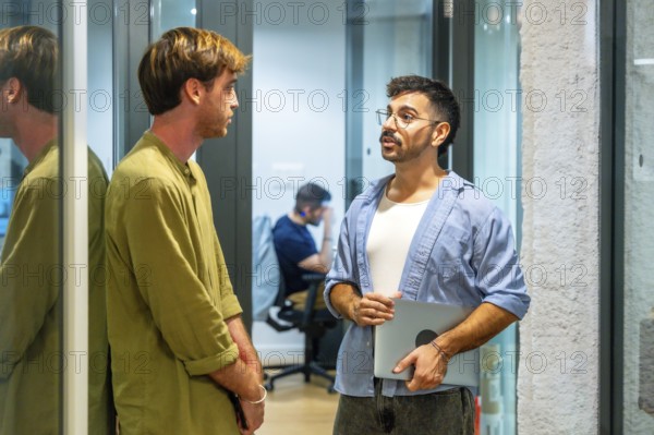 Two male colleagues engaging in an informal discussion during a break in a modern coworking space,