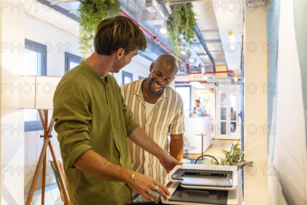 Male coworkers collaborating on a document at the printer, sharing a laugh and enjoying positive