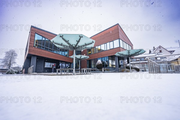 Modern town hall building with glass windows in winter surrounded by snow and cloudy sky,