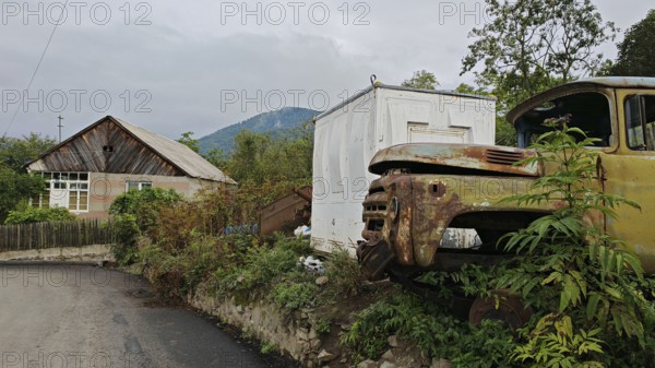 A rusty truck is parked in front of a small house on the side of the road in a village, retro