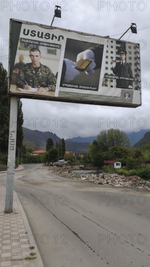 A large advertising poster on the side of the road, army looking for soldiers with mountains in the