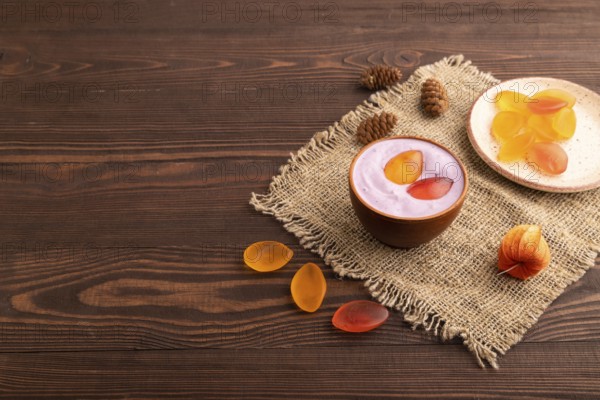 Purple Yogurt, with jelly candy on brown wooden background and linen textile, side view, copy