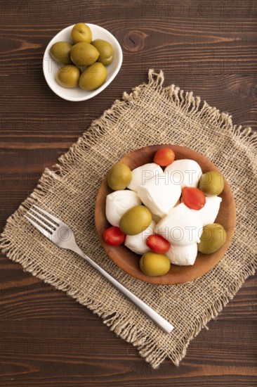 White Mozzarella cheese, with tomatoes and olives in wooden bowl on brown wooden background and