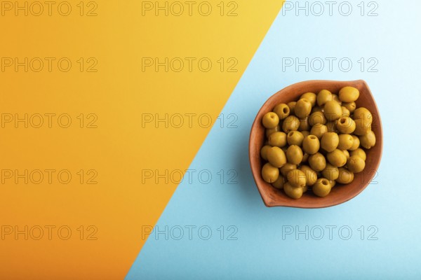 Fresh green olives in ceramic clay bowl on blue and orange pastel paper background. Top view, flat