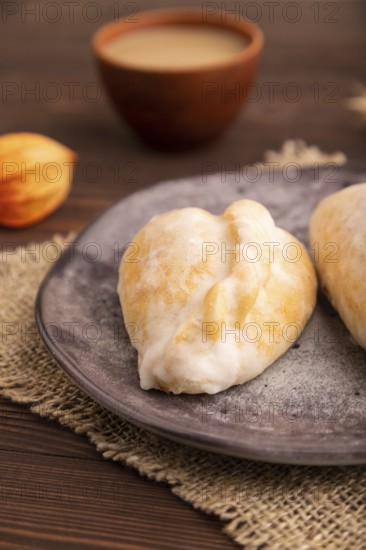 Glazed Pies with Cowberry jam on brown wooden background and linen textile, cup of coffee, side