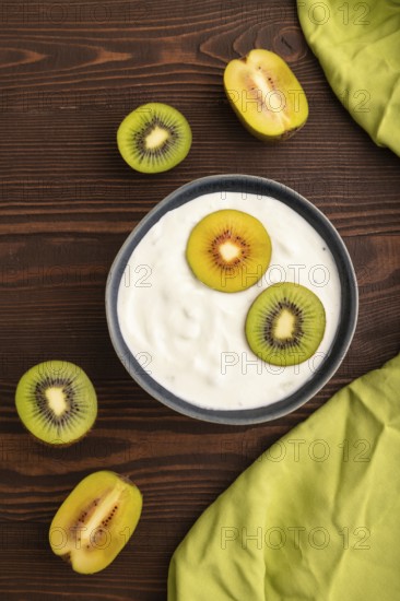 Yogurt, with kiwi in blue bowl on brown wooden background and green linen textile, top view, flat
