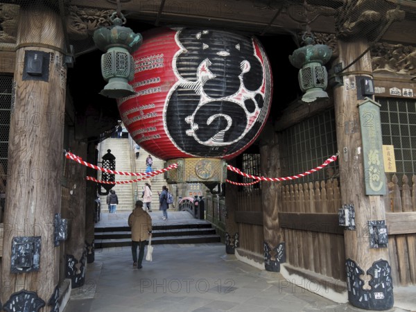 A large temple with an impressive lantern and traditional wooden construction, people enter the