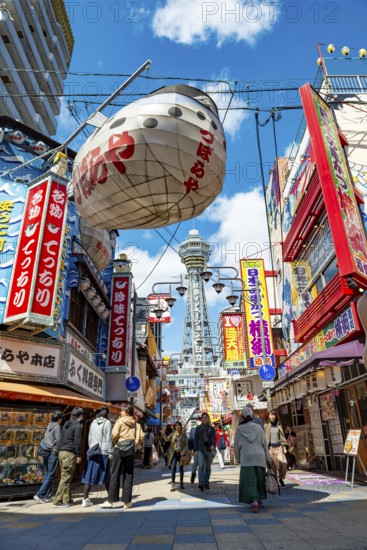 Lots of colorful signs in a pedestrian zone with shops and restaurants, behind Tsutenkaku Tower,