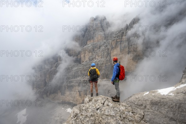 Climbers on the Via Ferrata Oliva Detassis via ferrata in fog, rocky mountain peaks and mountain