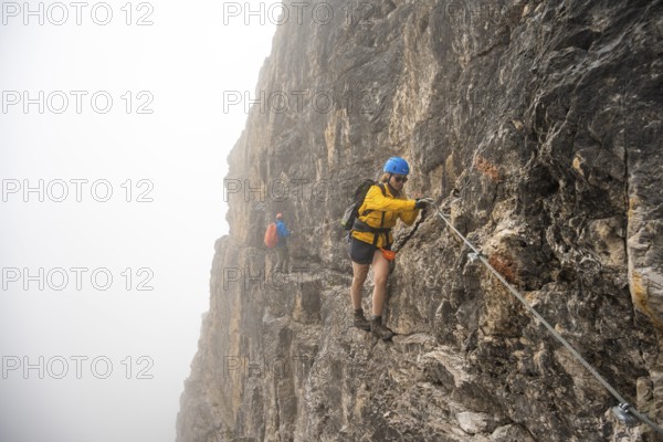 Mountaineers on a ladder on the Via Ferrata Oliva Detassis via ferrata in fog, rocky mountain peaks