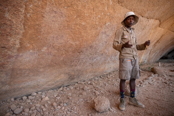 Bushman's paradise, guide standing in front of a massive red rock wall in a desert-like