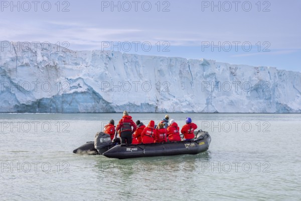 Eco-tourists in Zodiac boat from Poseidon Expeditions looking at Brasvellbreen glacier wall