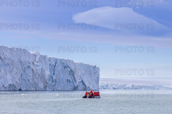 Eco-tourists in Zodiac boat and Brasvellbreen glacier wall from ice cap Austfonna debouching into