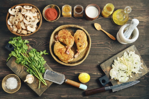 Top view of fried chicken thighs on a wooden plate. Chopped onions, mushrooms, and herbs are placed