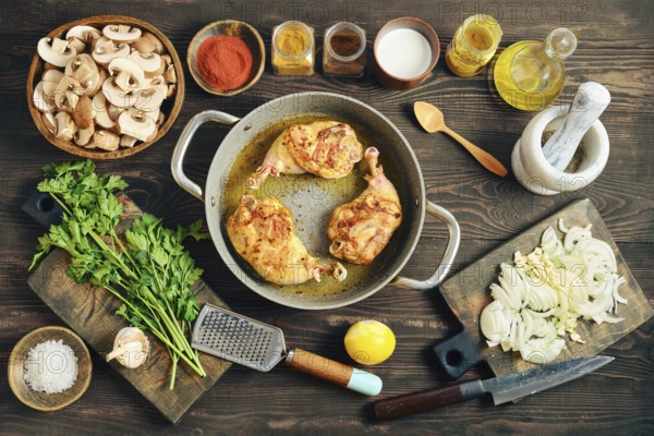 Roasted chicken legs in a pan on a wooden tabletop surrounded with mushrooms, onions, and various