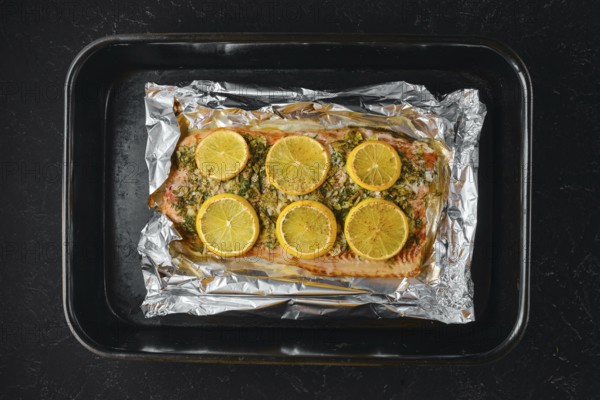 Pink salmon is placed on a baking sheet lined with foil. Lemon slices are arranged on top of the