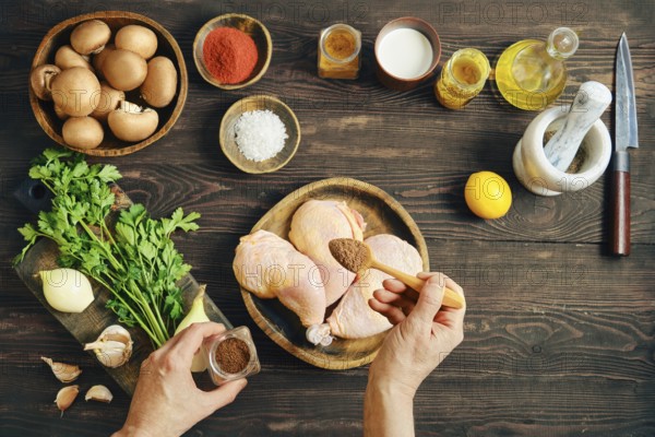 Top view of hands seasoning raw chicken legs with spicy pepper mix while preparing food on dark