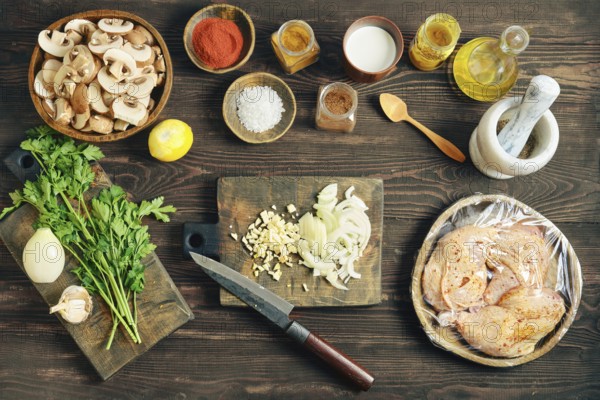 Top view of lifestyle food prep with sliced mushroom and wrapped chicken on a dark rustic wooden