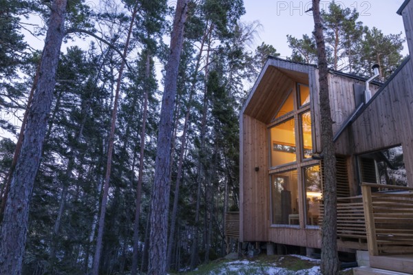 Modern wooden house in the forest, illuminated from within and inviting at dusk, Korpoström, Korpo