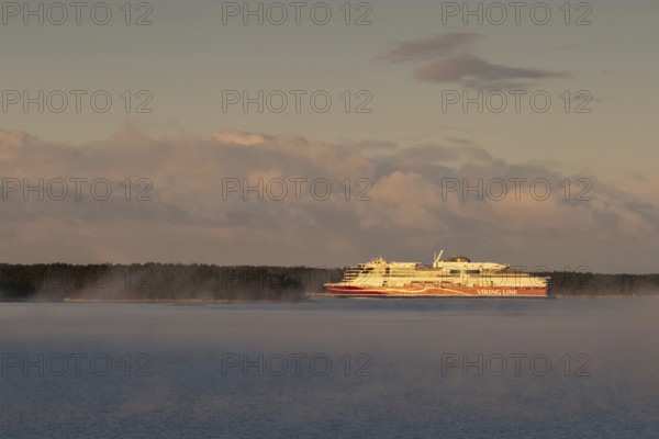 Large Viking Line ferry sails on the calm sea near a wooded shore at sunrise, Korpoström, Korpo or