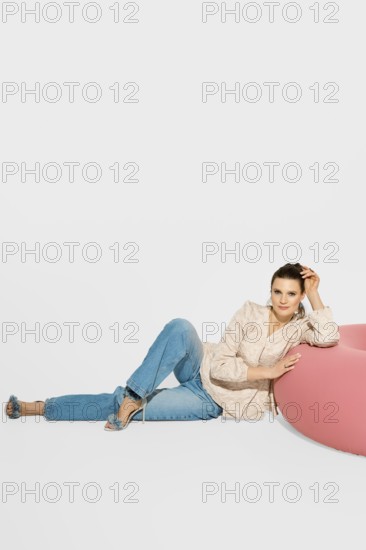 A woman is lying near a pink bean bag, leaning her torso back while resting on her left arm. She