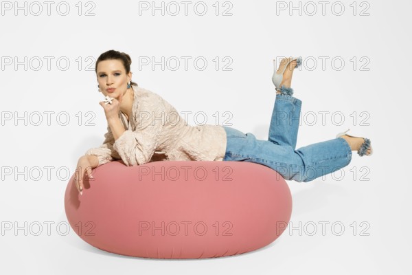A model lies on a pink bean bag in a studio. She is wearing casual clothes with flared jeans and