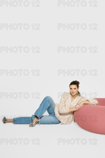 A woman sits on a floor near a pink piece of furniture in a bright studio. She leans back, wearing