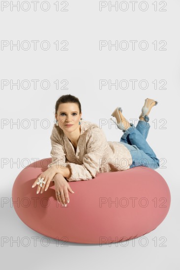 A woman lies on a pink bean bag with her legs raised and feet resting on the cushion. She wears a