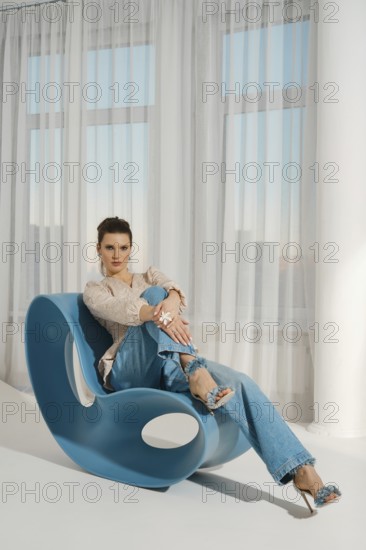 A woman is sitting on a blue chair. She is wearing casual clothes and is smiling. The room has a
