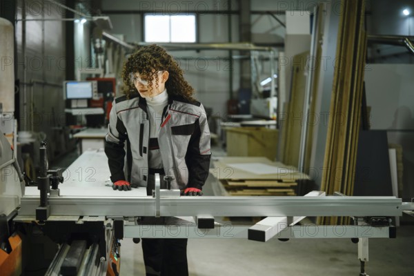 A person stands at a workbench in a workshop, preparing to cut wood. The space is filled with tools
