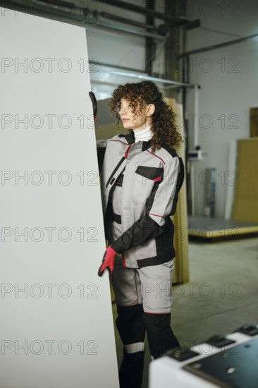 A woman is positioning a large wooden panel carefully in carpentry workshop. The area is filled