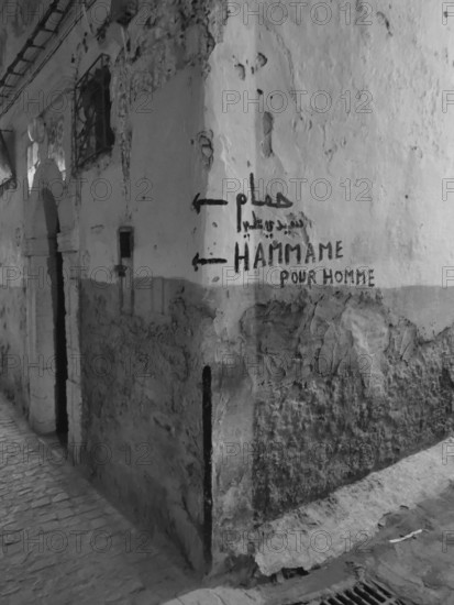 Dilapidated wall with graffiti and references to a hammam in a narrow alley, monochrome, old town