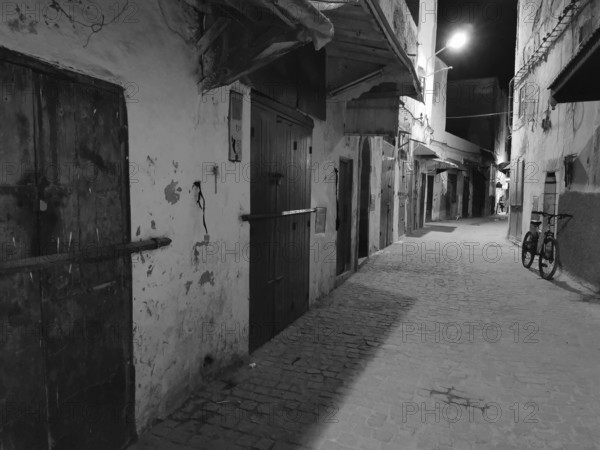 Nocturnal alley with a bicycle and closed doors in an urban setting, monochrome, old town of