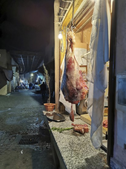 A piece of meat hangs in a shop window on a busy alley of an oriental market, Medina, at dusk,