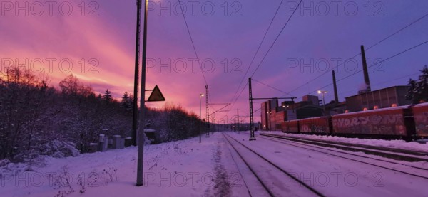 Sunrise at a snow-covered train station on Rennsteig, railroad tracks in purple sky with factory in