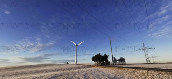 Winter landscape with wind turbine and power lines against a blue sky, Rennsteig, Frankenwald